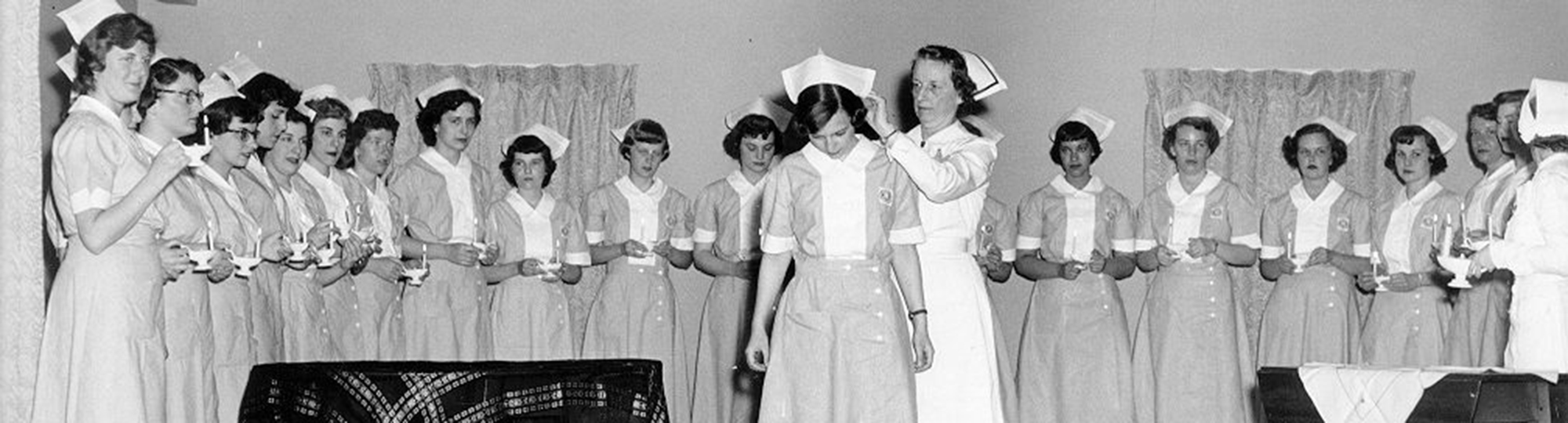 A black and white photo shows a group of nurses having hats pinned to their heads